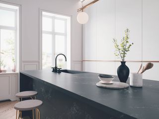 Dark kitchen island counter with wooden stools, back accessories, stainless steel faucet and a little greenery in front of large windows