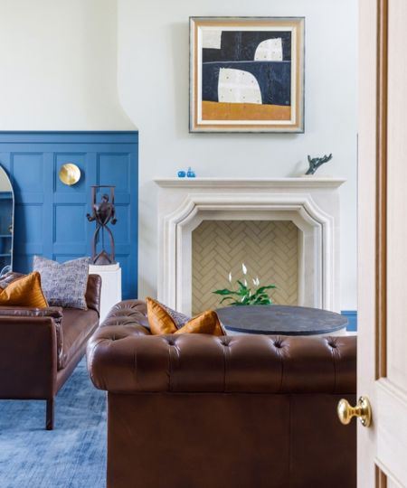 A living room with white walls, blue panels, dark brown couches, and a blue carpet, with a beige door to the right