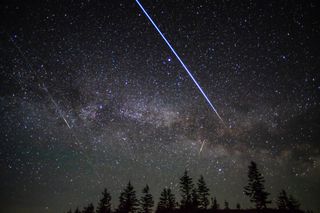 a streak of light zooms among the stars in the night sky