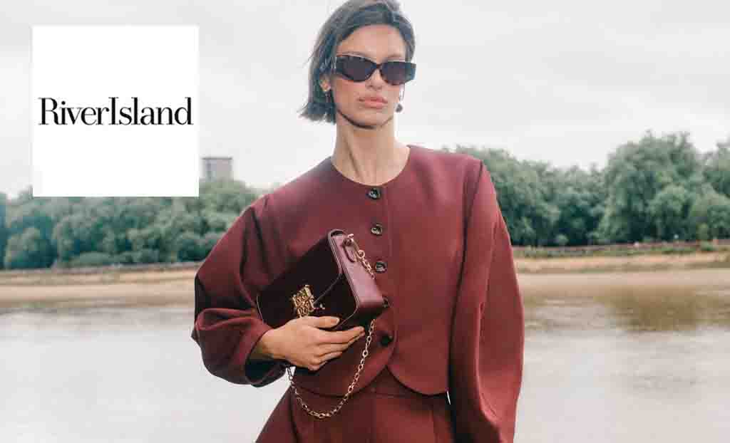 River Island logo placed over a woman with pixie cut wearing sunglasses a maroon outfit and bag 