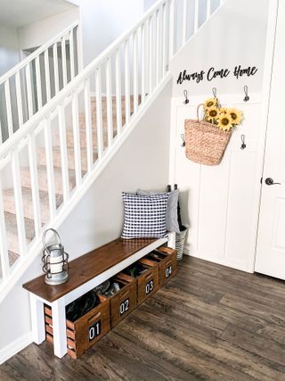 White entryway with stair banister wooden seat and small crates plus hooks with hanging wicker basket and flowers