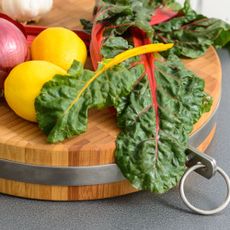 Rainbow chard leaves and lemons on wooden chopping board in kitchen