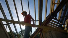 Builder carrying roof joist in unfinished house