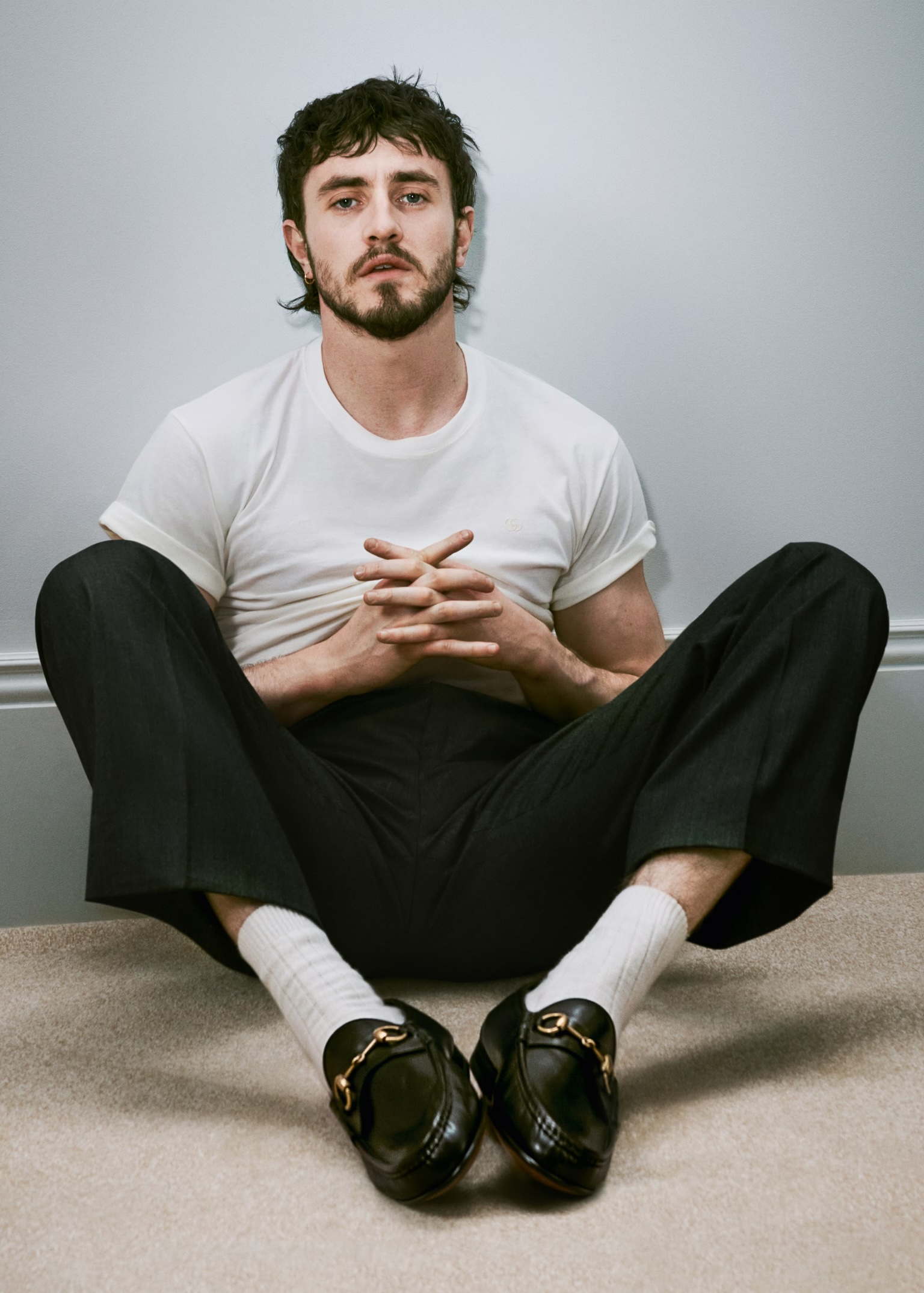Paul Mescal sitting on the floor in a white t-shirt, black trousers, white socks and black Gucci loafers