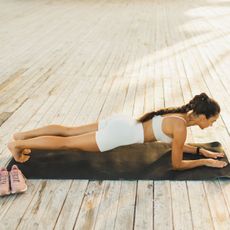 A woman doing a reverse plank variation, on a workout mat in gym gear