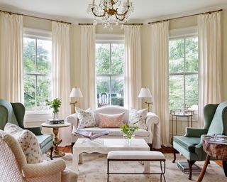 Living room with white sofa with throw pillows, green armchairs and patterned armchair, area rug and neutral walls and drapes