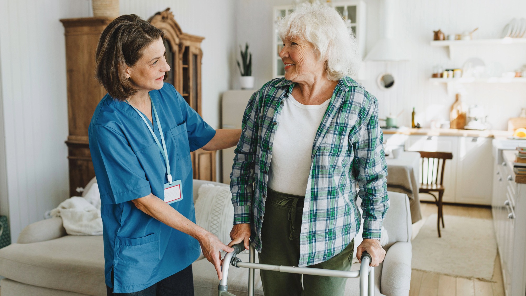 Carer helping elderly lady using walker at home