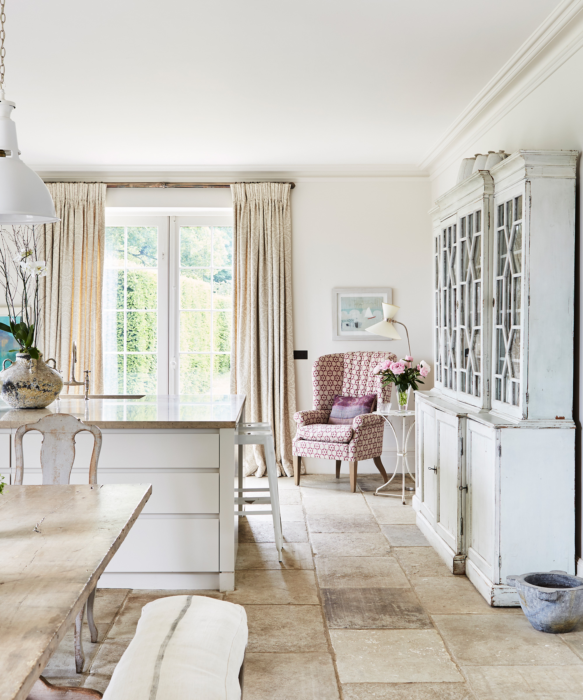 A large kitchen with stone flooring, a white island and a large kitchen dresser next to an armchair