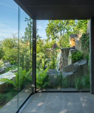 view from glass garden building of sloping garden with rock waterfall