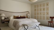 A neutral bedroom with a large brown and taupe fabric headboard, a white rugs, and rows of botanical prints on the wall