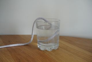 A glass of water with a cotton rope placed inside