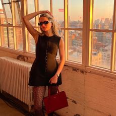@elizagracehuber wearing a black sculpted Tory Burch minidress with a red Prada handbag.