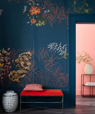 Dark, coral printed wallpaper ideas in the foreground, with a coral painted room through a doorway in the background.