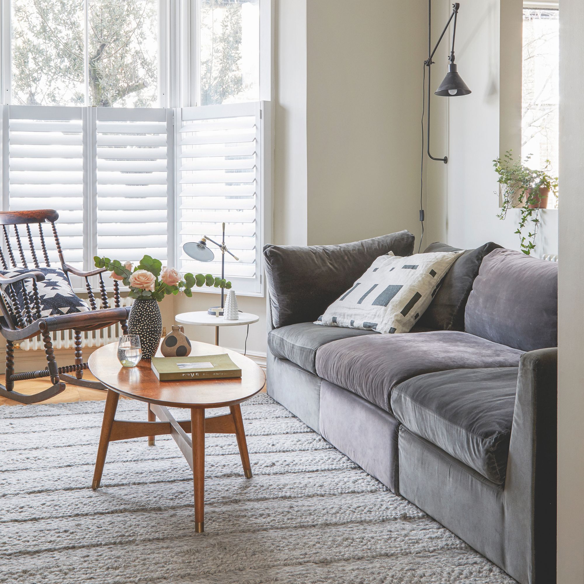 neutral painted living room with a grey sofa and wooden furniture, and a white rug on the floor
