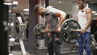 Man grimaces as he rows a heavy barbell in the gym