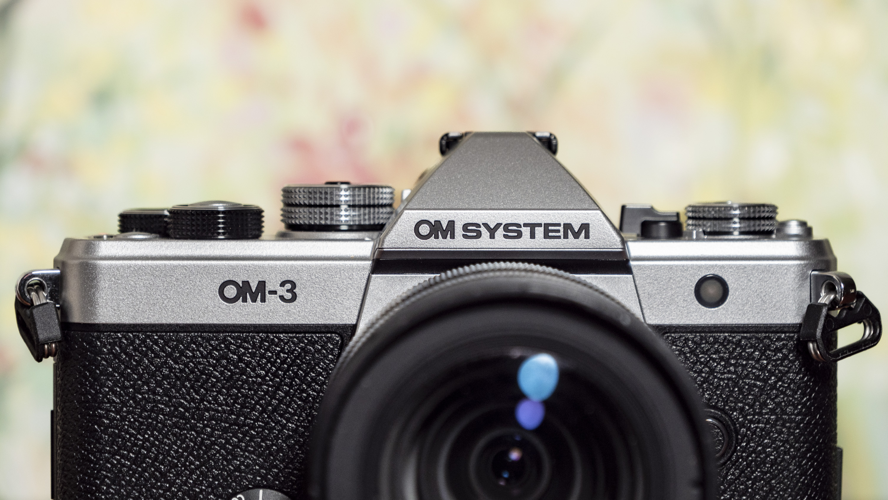 Top half of the OM System OM-3 mirrorless camera, floral backdrop