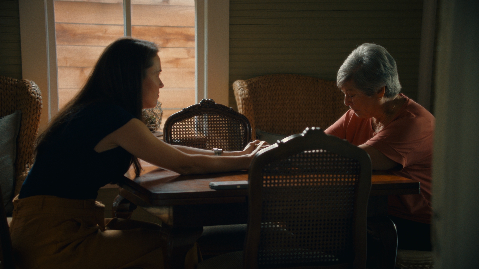 Sonora Thomas and Barbara Ayres-Wilson consoling one another over a dining room table in the yogurt shop murders