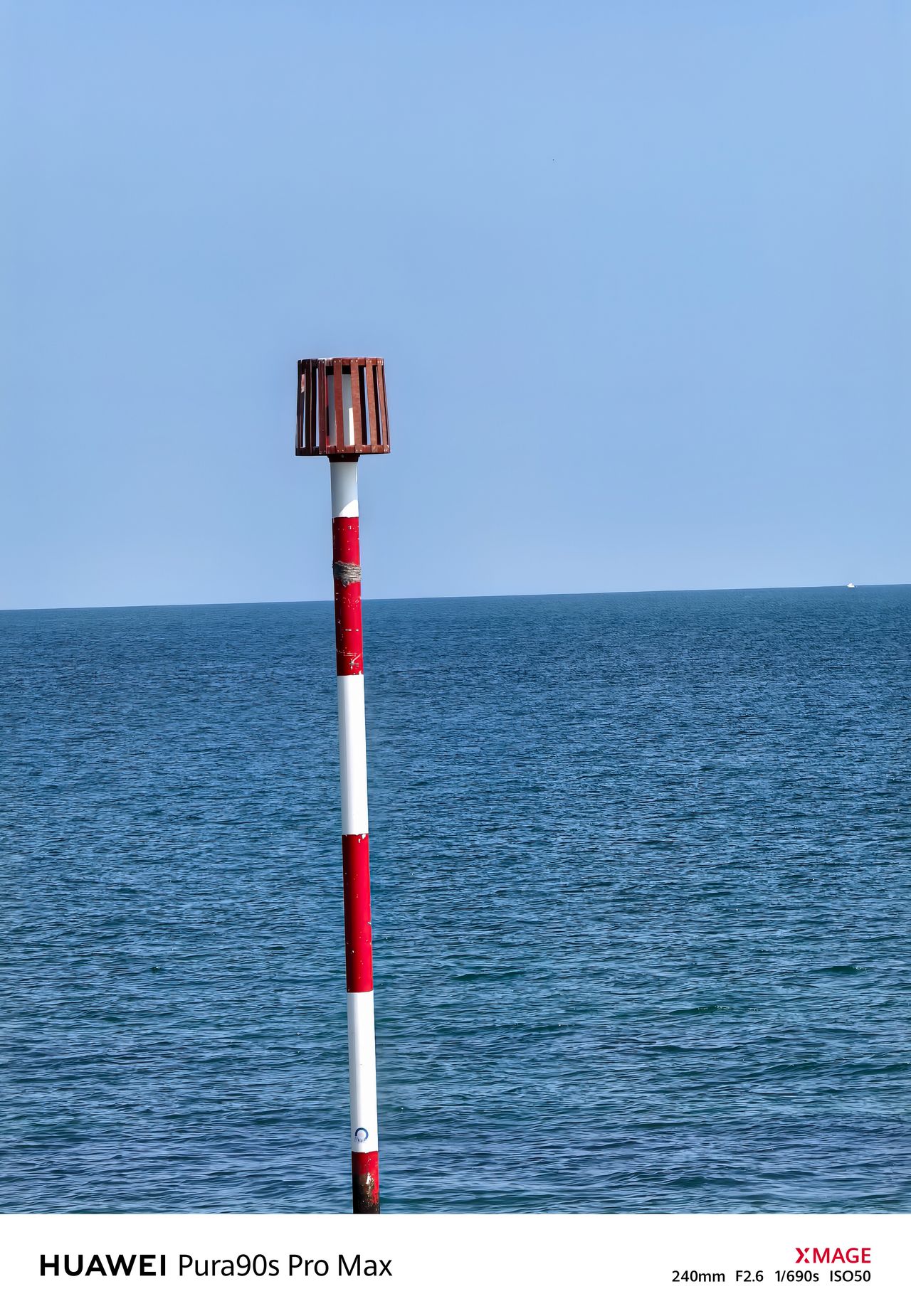 Close-up of a red-and-white striped navigation marker against the open sea and blue sky.
