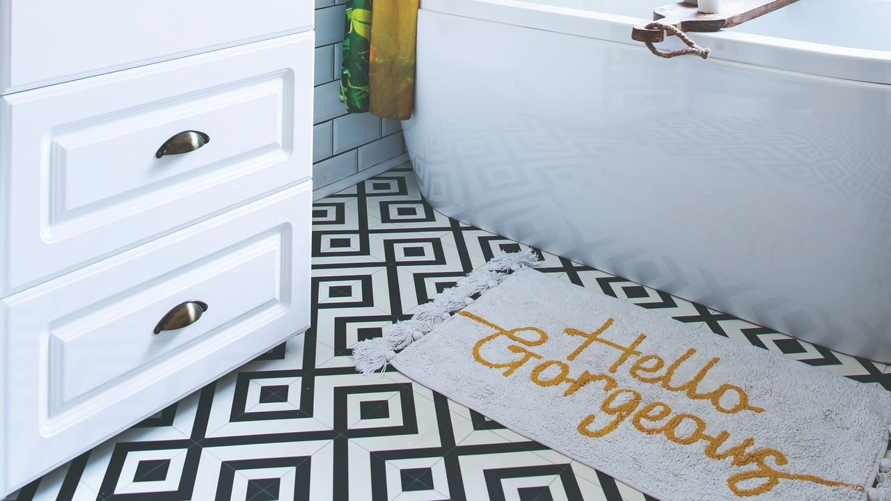 A bathroom with a graphic tiled floor and a slogan bath mat