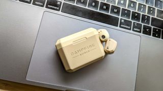 Campfire Audio Orbuds earbuds in ebeghe with closed charging case placed on a laptop keyboard