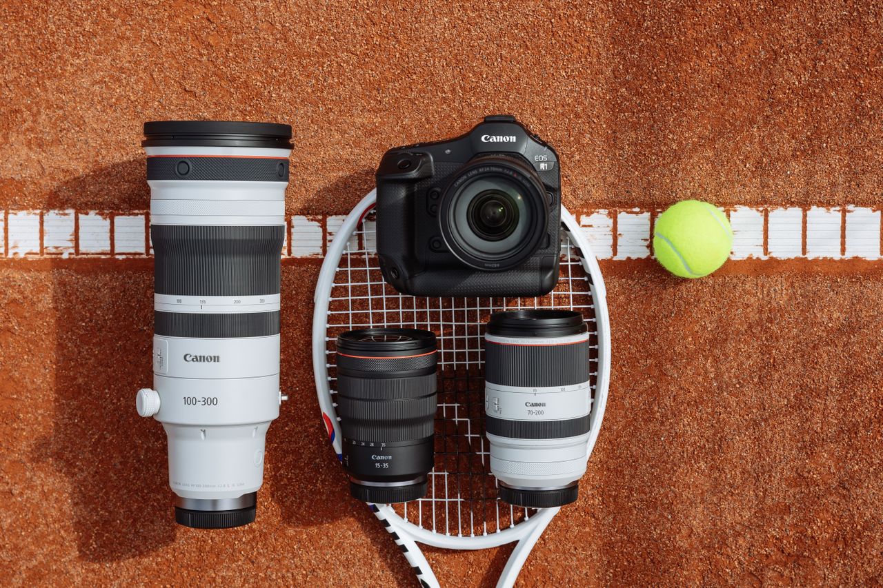 The Canon EOS R1 camera sitting on a court next to a tennis racket and lenses