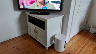Sonos Sub Mini står på gulvet foran tv-møbel med tændt tv.