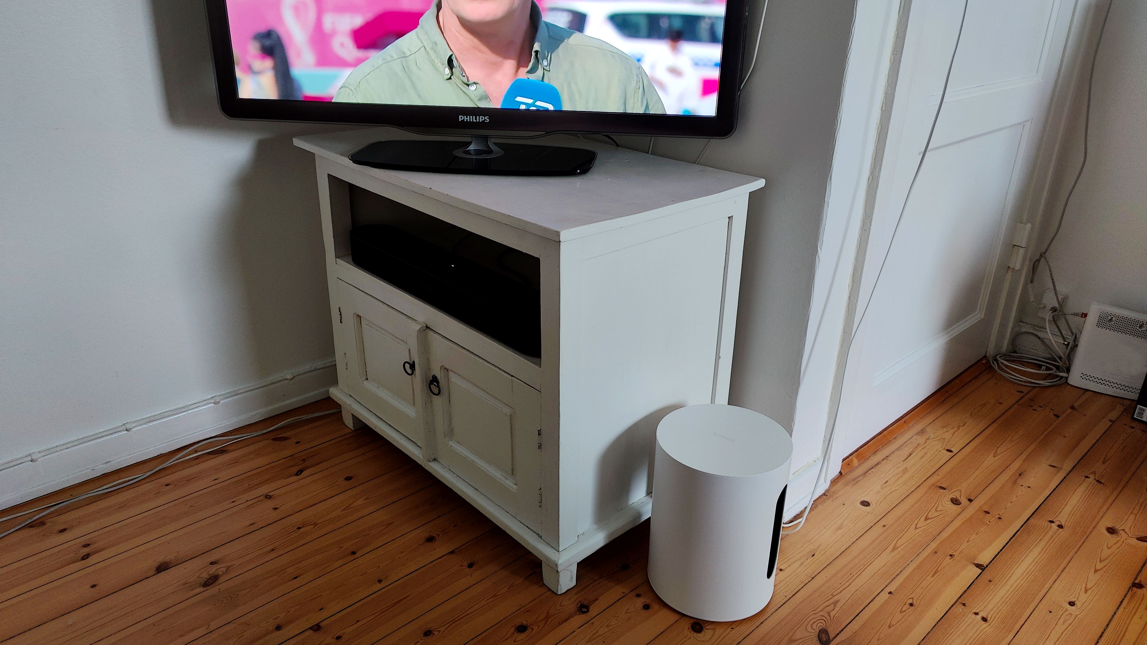 Sonos Sub Mini står på gulvet foran tv-møbel med tændt tv.