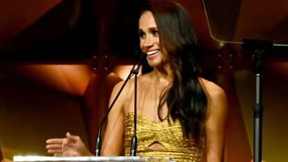 Meghan Markle in a gold gown speaking behind a podium