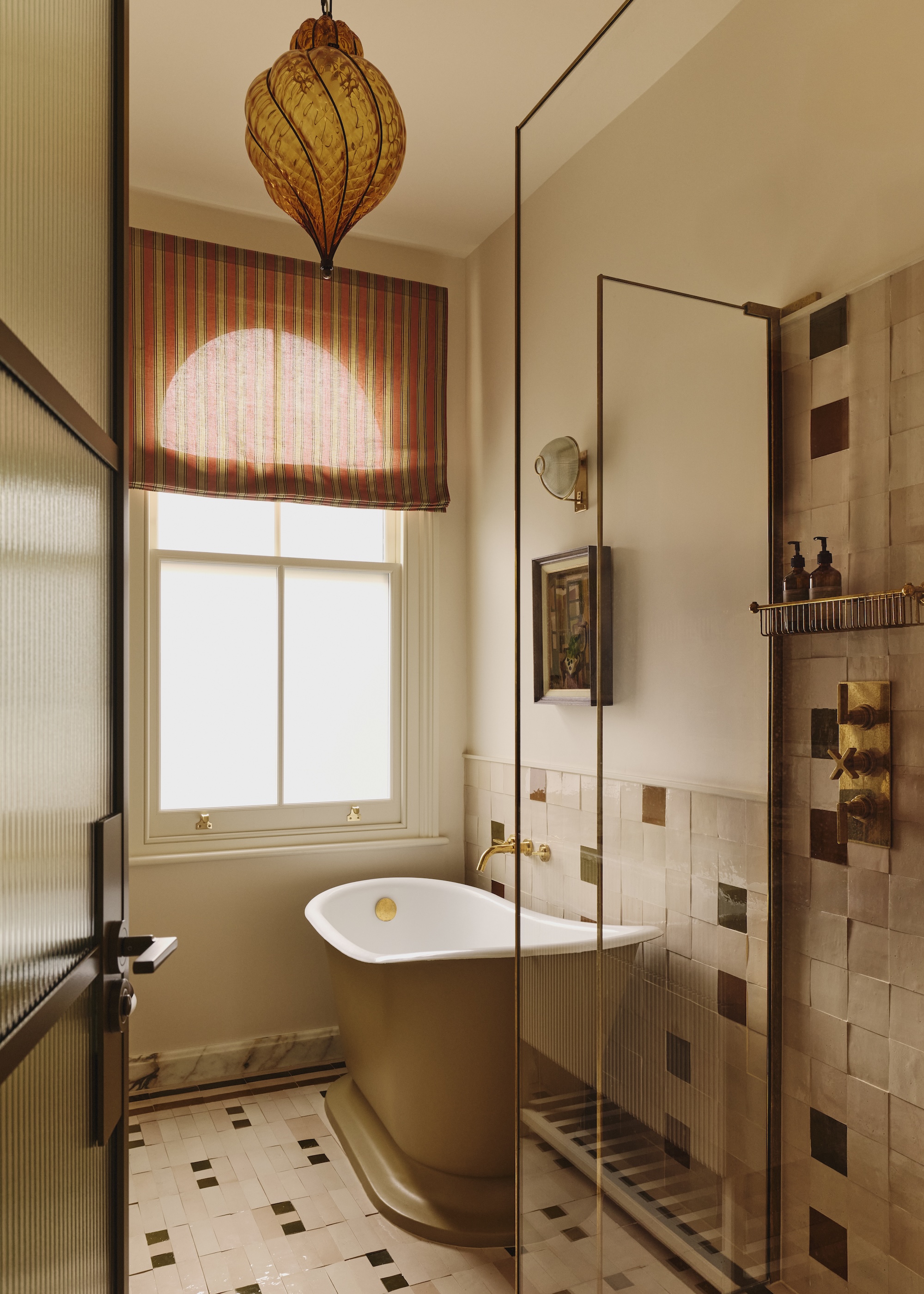 A compact bathroom with a roll top bath, muted earthy colors, a striped blind and a statement light in amber Murano glass