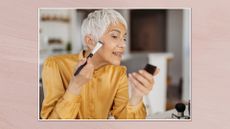 Side view of a woman with short grey hair applying makeup while looking into a small compact mirror