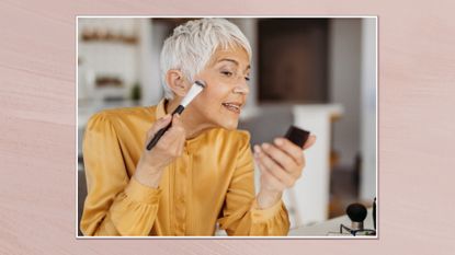 Side view of a woman with short grey hair applying makeup while looking into a small compact mirror