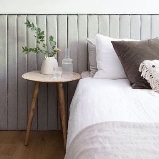 White painted bedroom with upholstered wall panelling headboard, wooden round side table