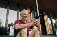 Mature man uses a phone while sitting on a cozy sidewalk cafe in summer