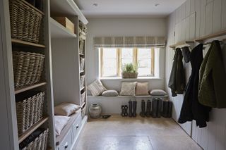 A country style mudroom with wicker basket storage, coat hooks and a bench with cushions