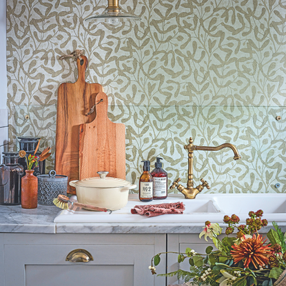 Kitchen sink and draining board in front of mistletoe wallpaper on a marble worktop with a stool decorated with flowers.