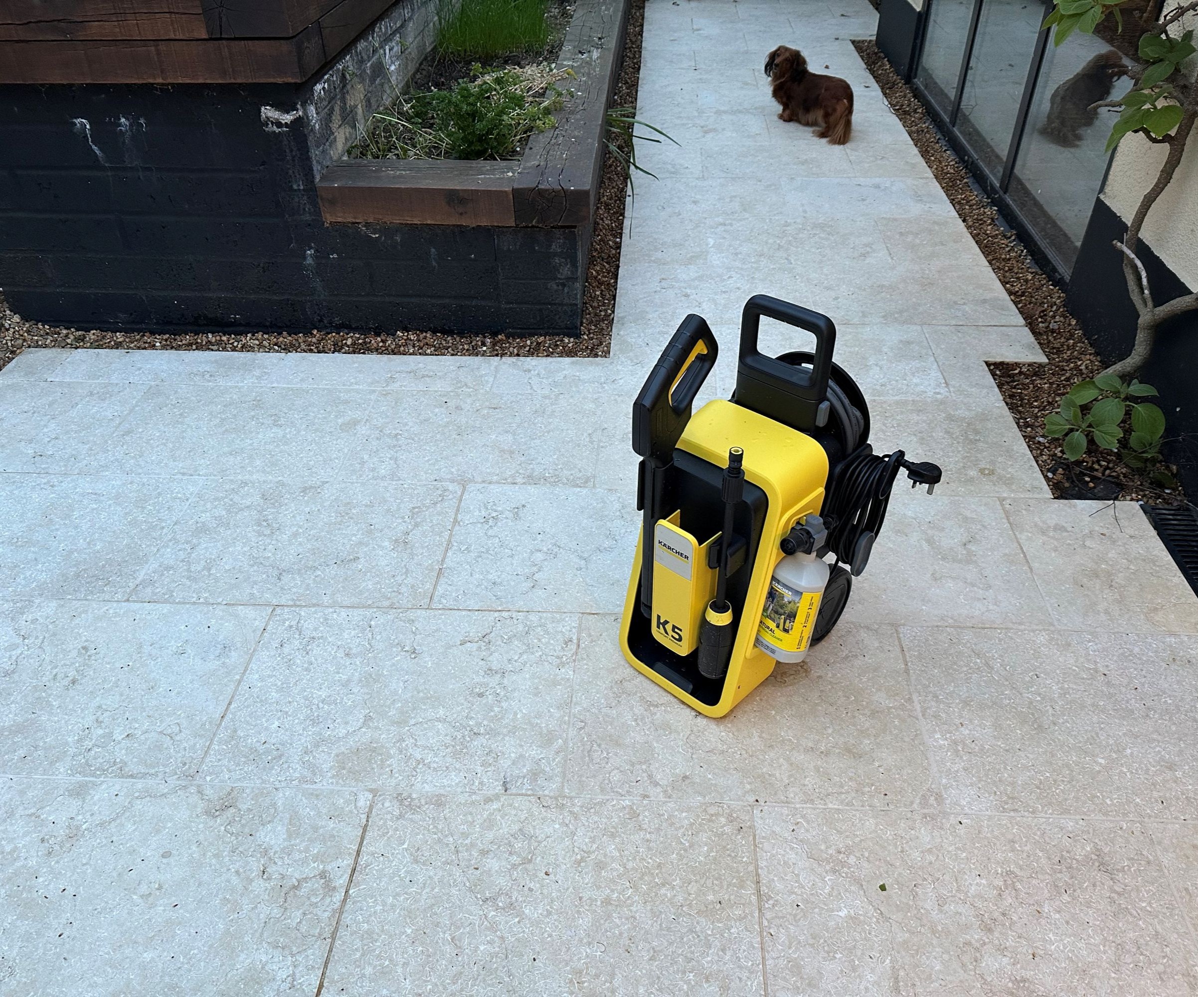 A yellow Karcher K5 Comfort Premium pressure washer on a cream limestone patio