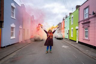 Woman in street with paint flare standing in between houses either side painted an array of colours