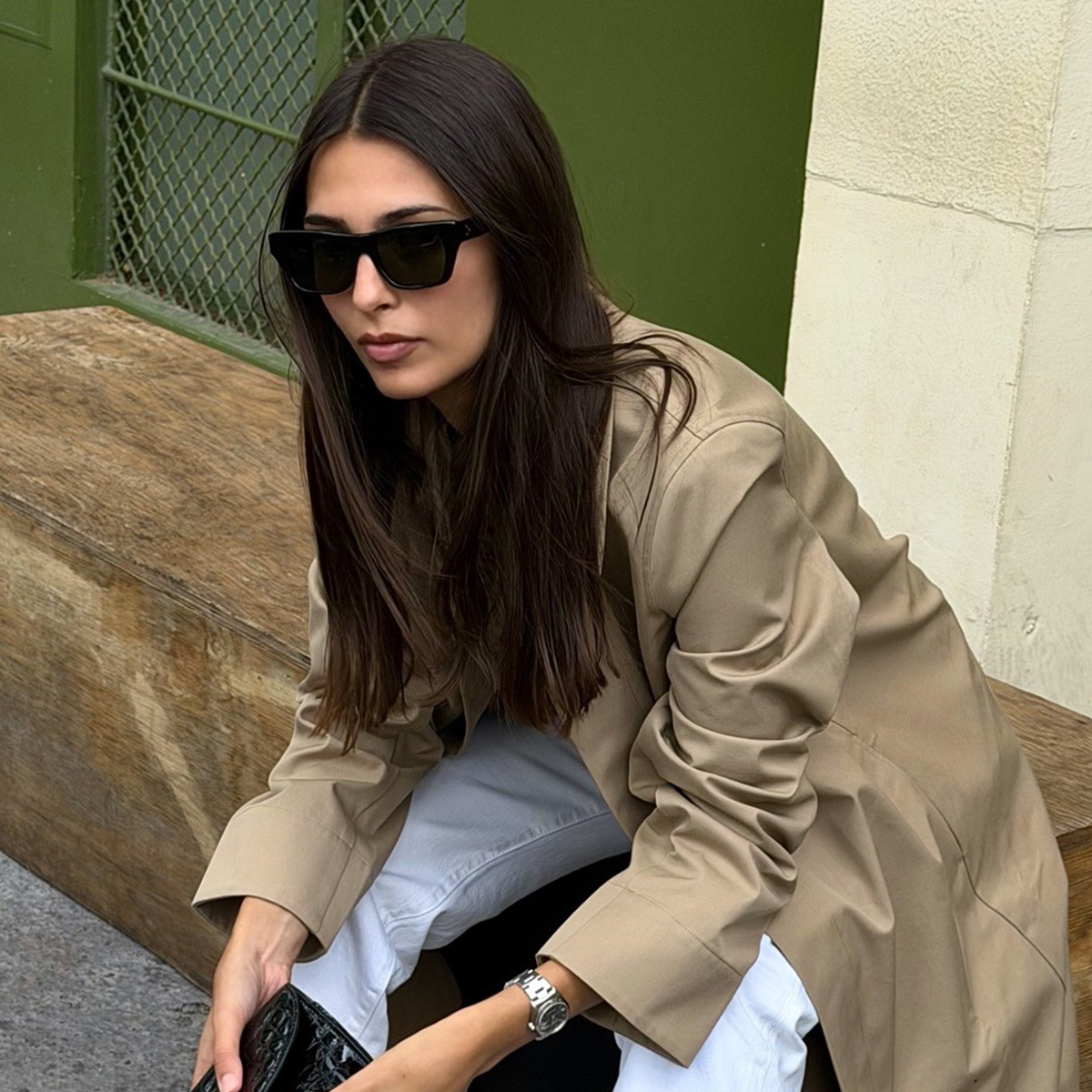 salome wears glasses, a trench coat, and white jeans.