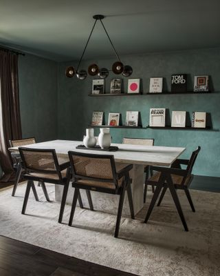 Dining table with teal plaster effect walls, white dining table and cane and black chairs
