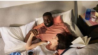 A couple relaxing on the Casper Dream, smiling at each other and holding a book and a cup of coffee