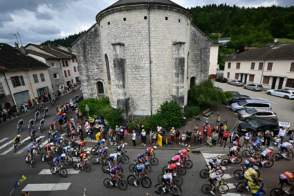 The pack of riders (peloton) cycles through Saint-Germain-de-Joux during the 20th stage of the 112th edition of the Tour de France cycling race, 184.2 km between Nantua and Pontarlier, in the Jura, eastern France, on July 26, 2025. (Photo by Loic VENANCE / AFP)