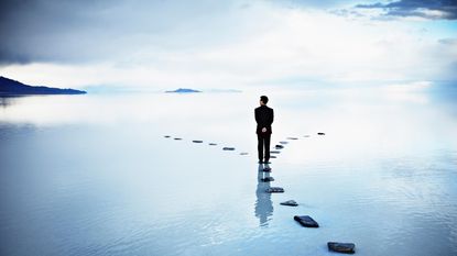 A man stands on a stepping stone where the path diverges ahead.