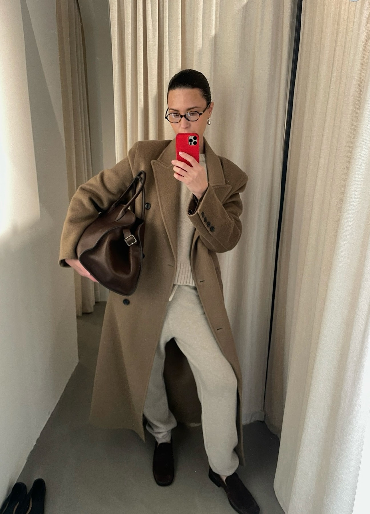 An image of @johannapiispa wearing a belted bag with a camel trench coat, grey sweatpants and suede loafers.