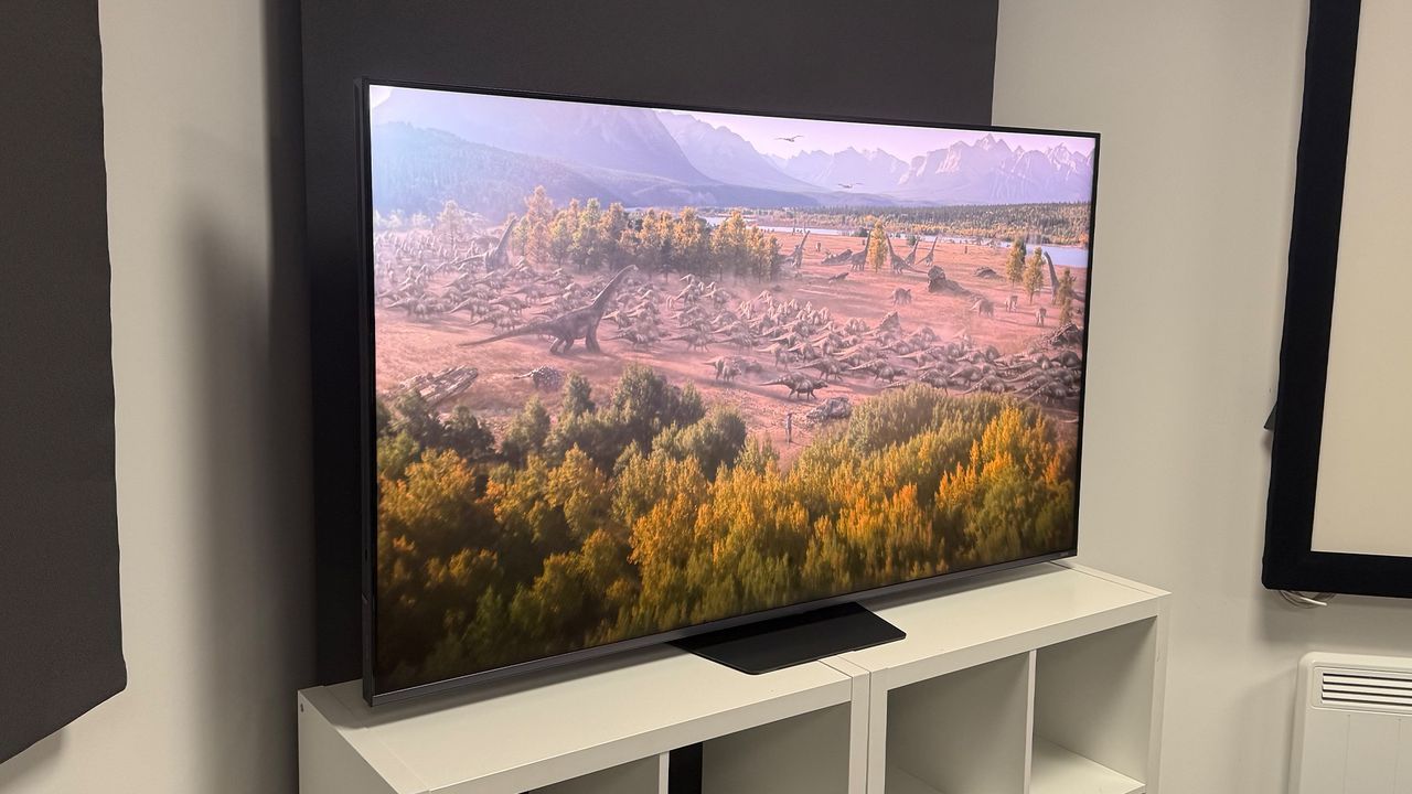The 65-inch Hisense UR9 RGB Mini LED TV, photographed on a white, wooden unit. On the screen is a still from Netflix documentary, The Dinosaurs.