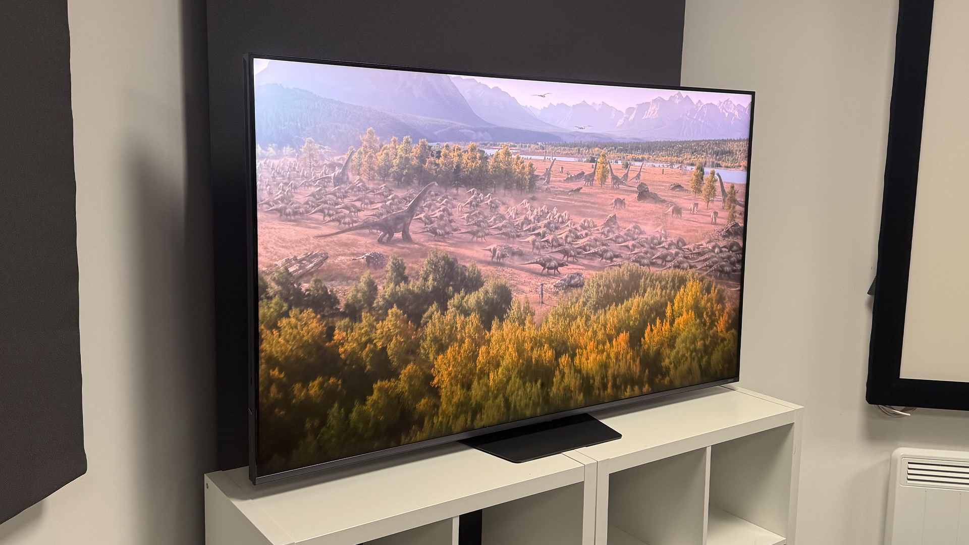 The 65-inch Hisense UR9 RGB Mini LED TV, photographed on a white, wooden unit. On the screen is a still from Netflix documentary, The Dinosaurs.