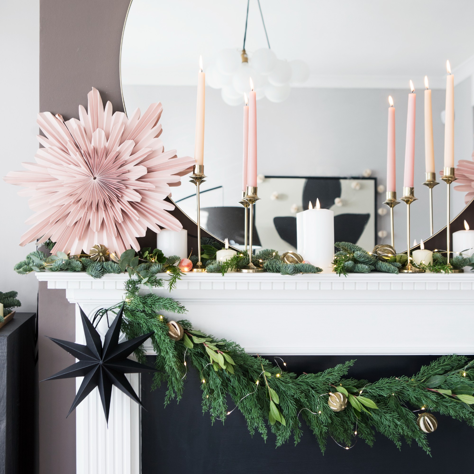 A fireplace mantelpiece decorated with a Christmas garland and two paper Christmas stars