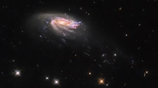 a pinkish jellyfish-shaped spiral galaxy imaged by the hubble space telescope