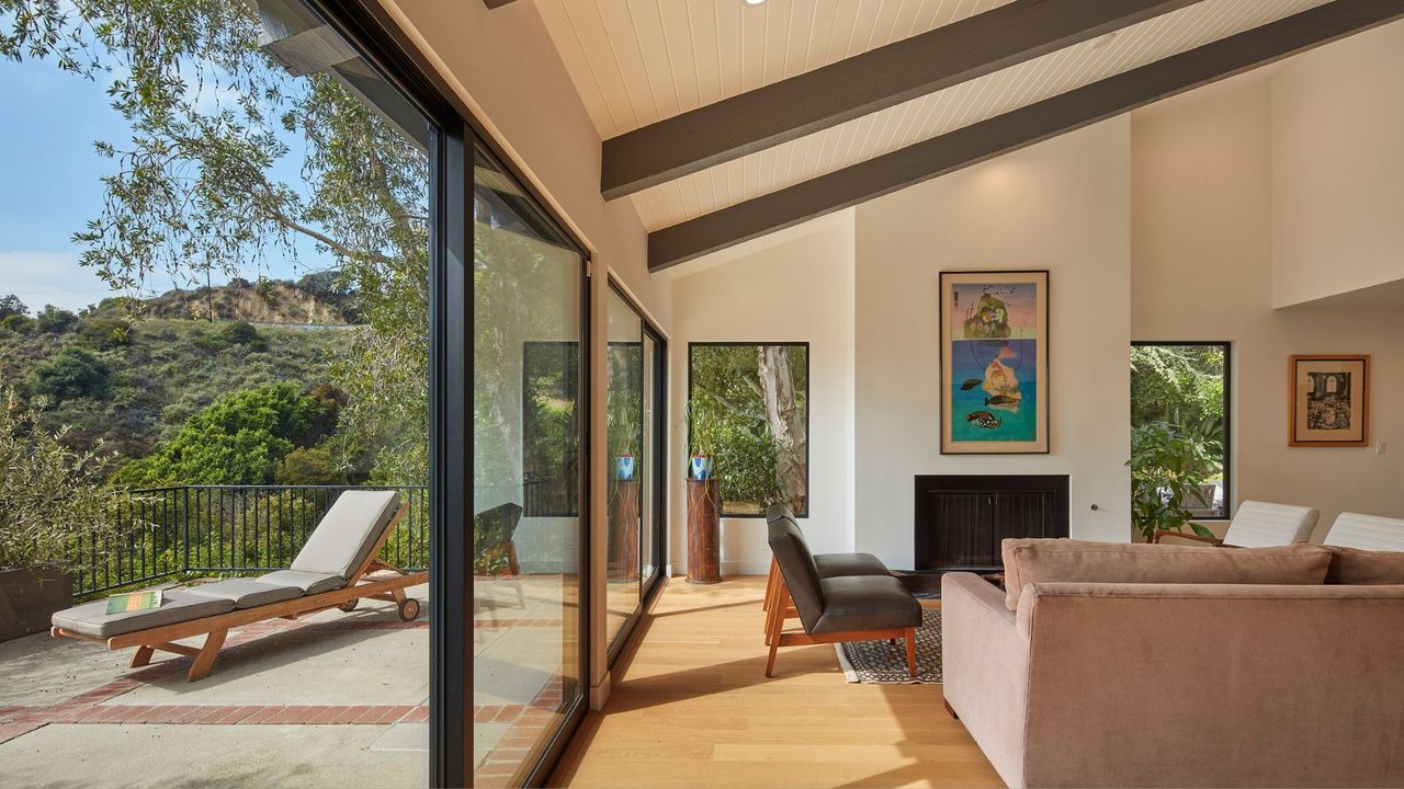 A living room with floor to ceiling windows leading to a balcony with a sun recliner