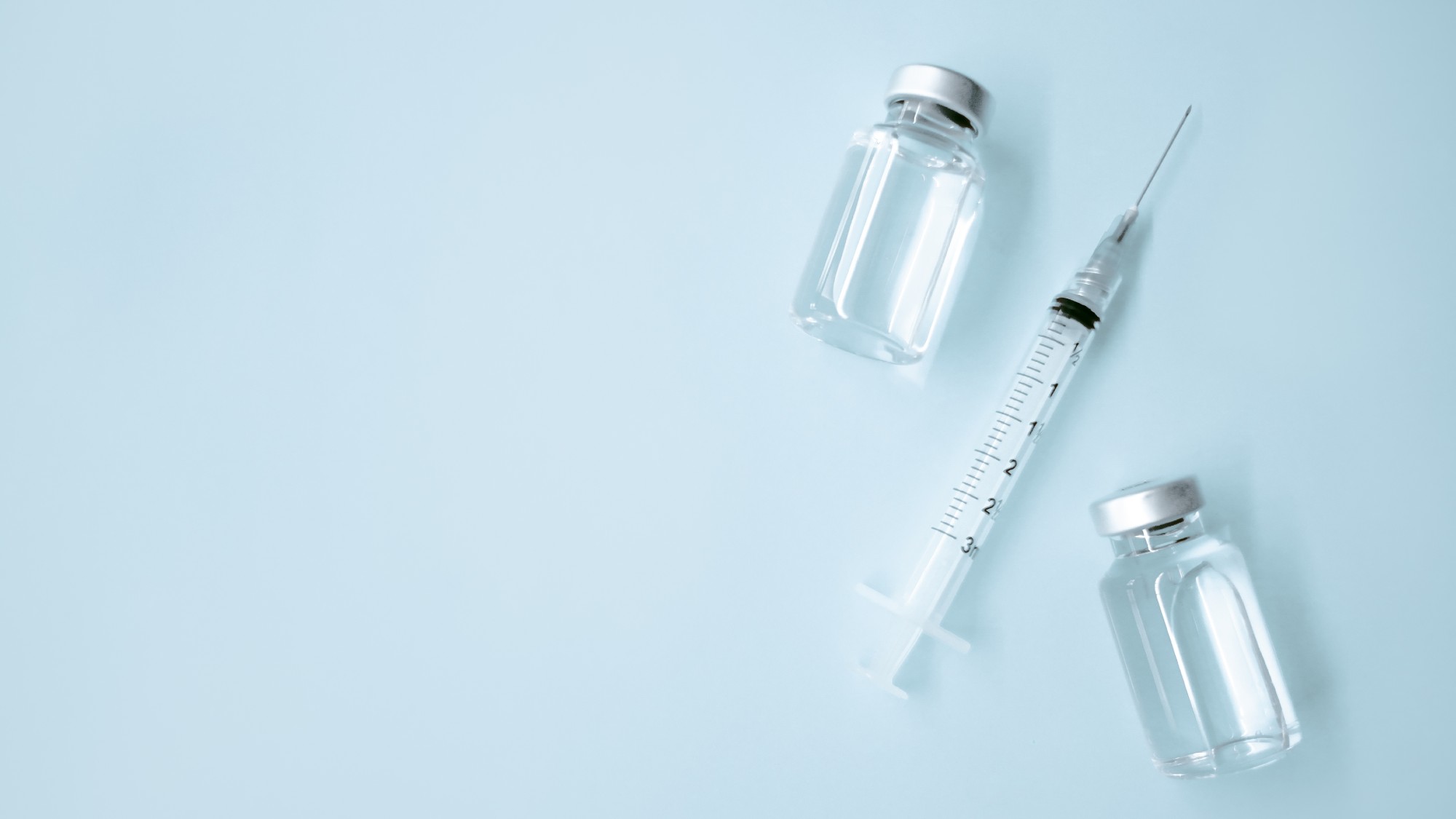 High angle view of syringe with needle and two medical vials on blue background