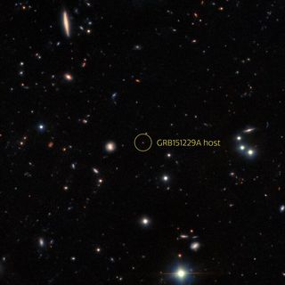 A deep view of space shows many distant stars and galaxies, including a previously hidden dim and distant galaxy thought to be the origin point of a powerful gamma-ray burst.